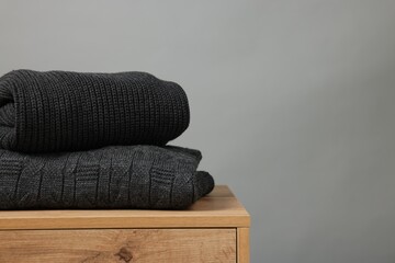 Stack of knitted sweaters on wooden table against grey background. Space for text