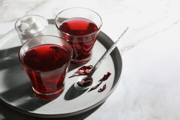 Delicious hibiscus tea, sugar cubes and dry roselle petals on white table. Space for text