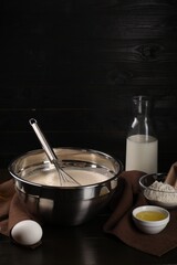 Composition with whisk and dough in bowl on table against dark wooden wall, space for text