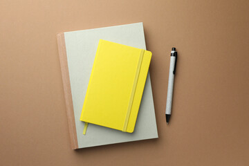 Different notebooks and pen on light brown background, top view