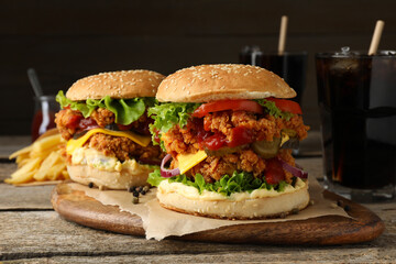 Delicious burgers with crispy chicken patty, french fries and soda drinks on wooden table