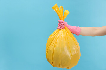 Woman holding plastic bag full of garbage on light blue background, closeup. Space for text
