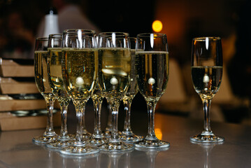 Champagne Toast Ready for Celebration Event. Glasses of sparkling champagne lined up on a bar counter, awaiting a festive toast at an evening event.