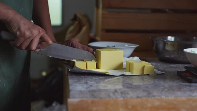 Hard stick of butter being cut to smaller cubes, filmed as medium close up slow motion shot