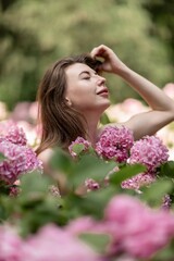 Fototapeta premium Hydrangeas Happy woman in pink dress amid hydrangeas. Large pink hydrangea caps surround woman. Sunny outdoor setting. Showcasing happy woman amid hydrangea bloom.