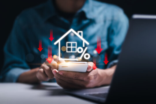 Businessman use smartphone with virtual home icon and down arrow for economical real estate and lower mortgage interest rates. Reduced prices for rental housing, Demand for home purchases decreases.