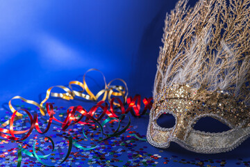 Golden Mardi Gras or carnival face mask with feathers on a blue background with colored tinsel and...