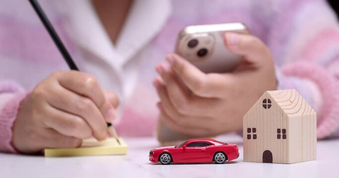 Close-up of an individual calculating finances on her car and house loans using a pencil, paper, and a mobile phone as calculator.