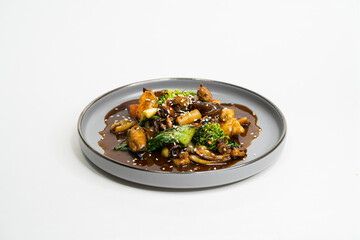 fried Asian dish with sweet and sour sauce, garlic and vegetables on a plate, side view