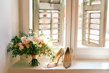 Bride high-heeled shoes along with a bouquet of flowers stand on the windowsill in a hotel room