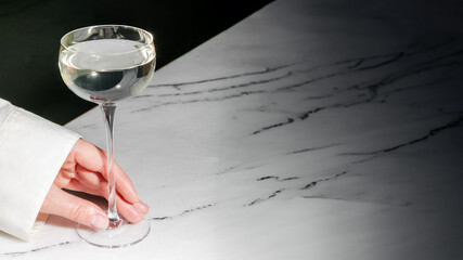 Elegant hand holding a glass of white wine on a marble countertop, suitable for concepts related to...