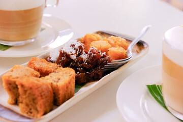 Close up view of plated cake snacks or kuihs, served with cappuccinos. This selection of delicious kuihs are typical Malay and Peranakan delicacies in Singapore and Malaysia