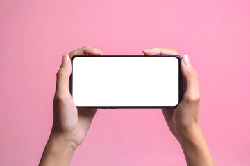 Two hands holding smartphone with blank screen mockup frame, isolated on pink background.