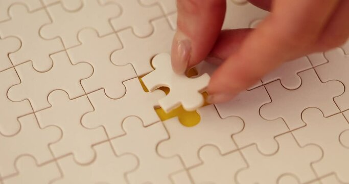 Woman hand inserts last piece of white puzzle into picture