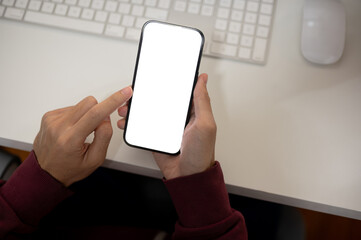 Top view image of a man using his smartphone at her office desk. A white-screen smartphone mockup