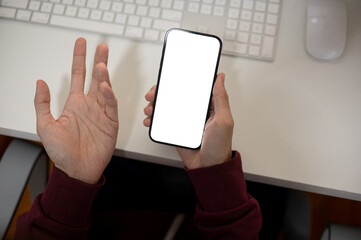 A dissatisfied male office worker is checking messages on his smartphone at her office desk.