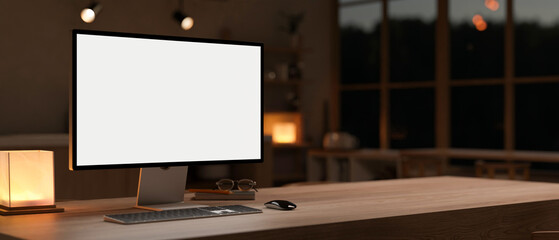 A PC computer mockup on a hardwood table in a cosy, modern room at night. dark workspace concept