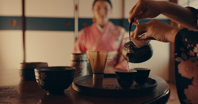 Woman pouring traditional Japanese tea with kimono, teapot and relax with mindfulness, respect and service. Girl at calm tearoom with matcha drink in cup, zen culture and ritual at table for ceremony