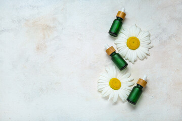 Composition with bottles of essential oil and chamomile flowers on light background