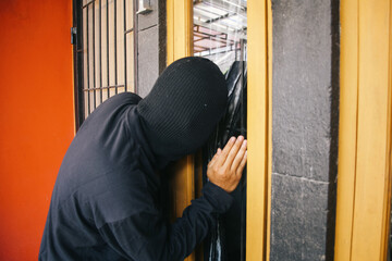 Burglar wearing a balaclava peeking and looking through the house window. Criminal and security...