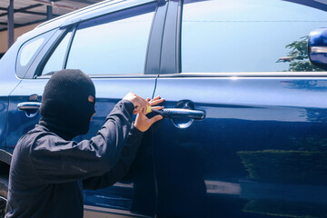 Theft with mask trying to break into the car using screwdriver. Street criminal and car theft concept. - obrazy, fototapety, plakaty