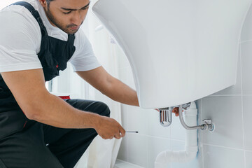 A skilled plumber uses a wrench fixing a water pipe under a bathroom sink. His repair service...