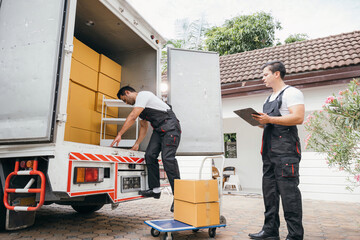 Two employees of a removal company work together unloading furniture and boxes from the truck...