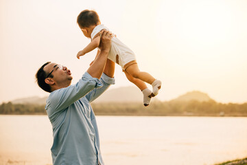 A happy dad and his toddler son share a playful moment of freedom and joy in the park, throwing him up in the air on a sunny summer day. Family love and happiness captured in a photograph - obrazy, fototapety, plakaty