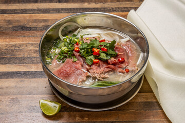 Hanoi rare Beef Pho topping with onion, noodles, green onion, red chilli, lemon and coriander served in bowl isolated on wooden table top view of hong kong fast food