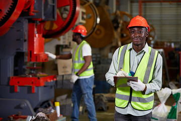 African factory worker or engineer writing on clipboard beside machine in the factory