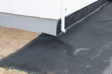 Laying a black waterproofing membrane around the foundation of a house. Construction of the blind...