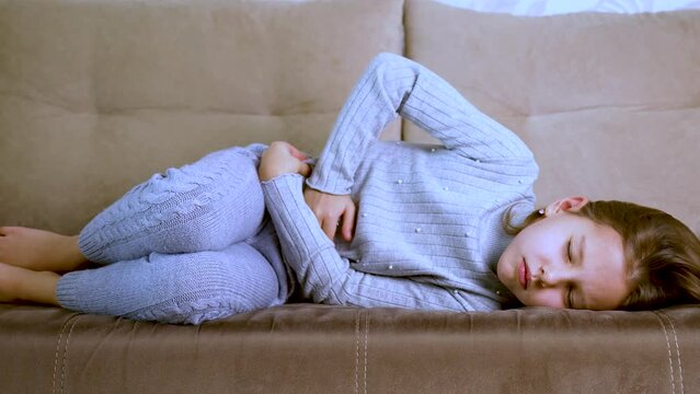 Little girl lying on a sofa and holds her stomach
