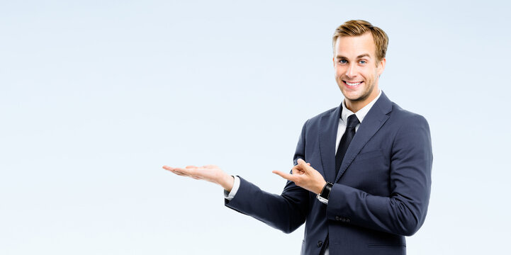Businessman in suit showing, holding, giving some product or free copy space area for advertising text, isolated grey wall background. Happy corporate business man at studio image. Professional person