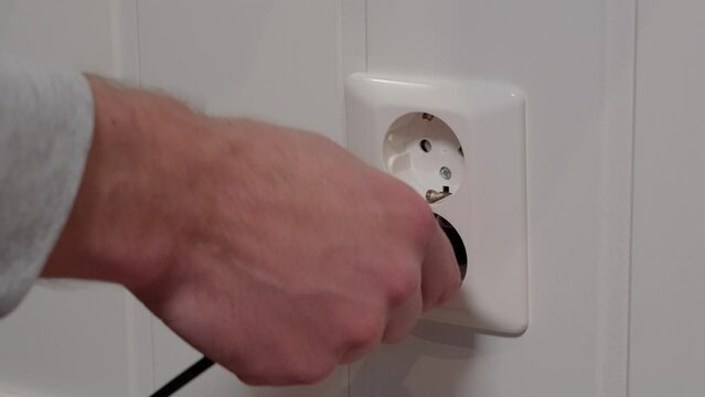 Male hand plugging electric cord into 230 volt socket, close up low angle