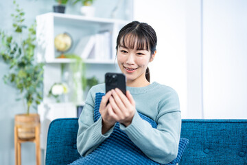 部屋のソファで携帯を持つ私服の若い女性