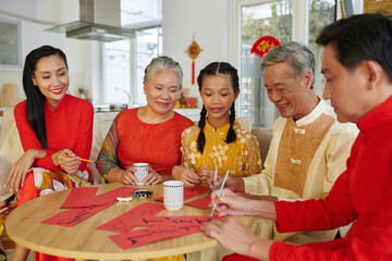 Cheerful big family writing couplets on red paper for Lunar New Year celebration
