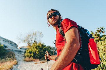 Young man hiker travels through the mountains with trekking poles for nordic walking