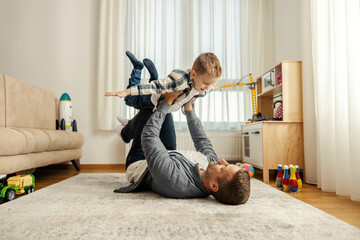 A father and son are playing airplane at home.