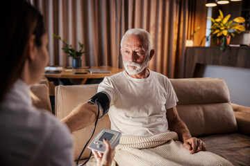 A family doctor is measuring blood pressure on her senior patient during home visit.