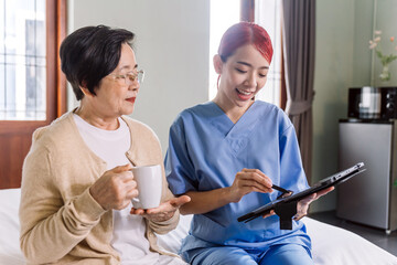 Asian woman nurse wearing scrubs report the health status of Senior Asian woman with digital tablet...