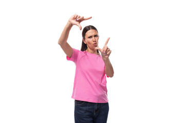 young positive good-looking woman with black hair dressed in a pink t-shirt makes a frame from her hands