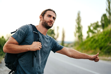 Young man hiker with backpack on hitchhiking near the road