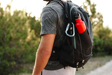 A male traveler backpack with mountaineering carabiner and thermos close up - obrazy, fototapety, plakaty