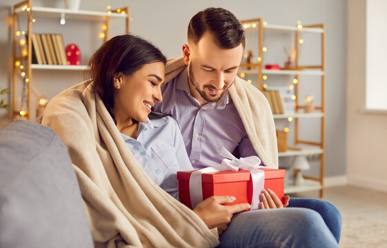 Loving couple close with gift box, pair in love under warm cozy blanket, male, female romantic Valentine day emotion. Festive present in affection on holiday, smiling male, female pair holding present