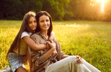 Portrait of a mother and child in nature. Happy little daughter together with her mom sitting on a...