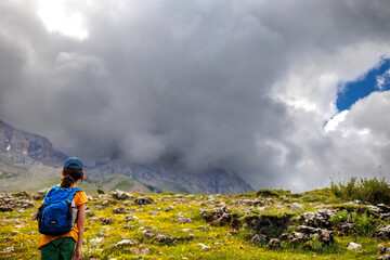 traveler child with backpack relaxing outdoors with rocky mountains in the background.