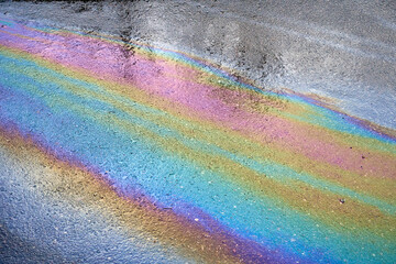 Gasoline spot on wet asphalt. Multi colored oil spill on asphalt road, abstract background, texture.