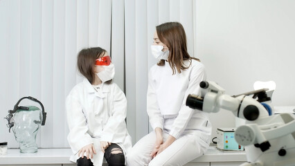 A candid emotional photograph of a child sitting in a dental office in a medical gown next to a young woman professional dentist.