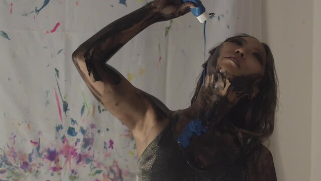A stunning Asian female model is pouring blue body paint on herself