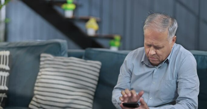 Asian Indian Hindu elder older tensed man sitting alone sofa couch talk phone call hold mobile feel bad think lonely indoor home aged old sad grief unwell male suffer health illness issue room house